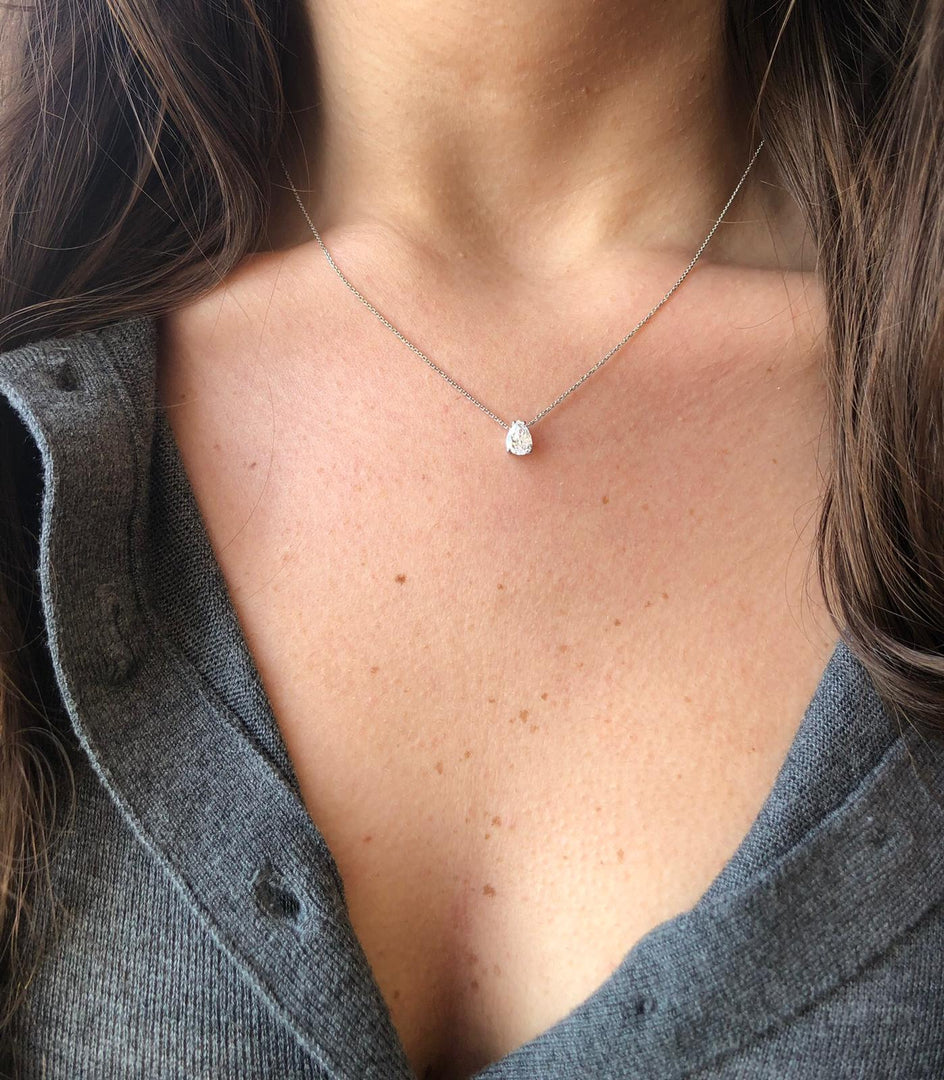 A close-up view of a woman's neck and chest area, showing a delicate necklace with a small diamond pendant.
