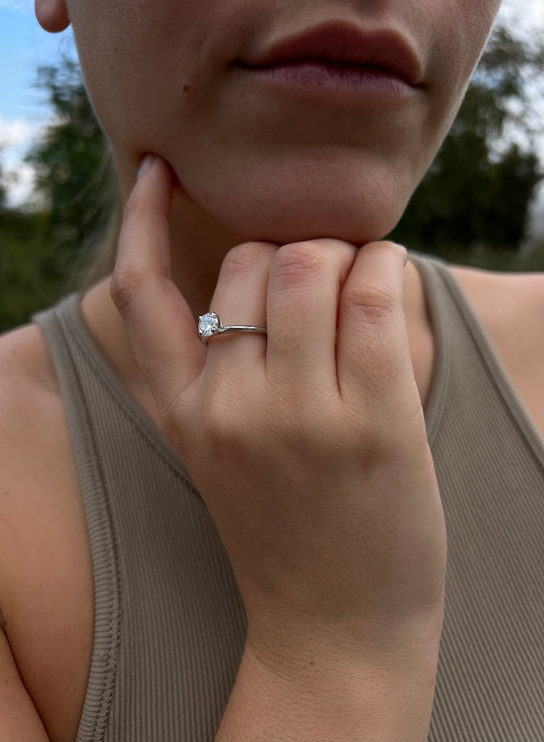 A close-up of a person's hand wearing a diamond engagement ring, with a thoughtful expression on their face.