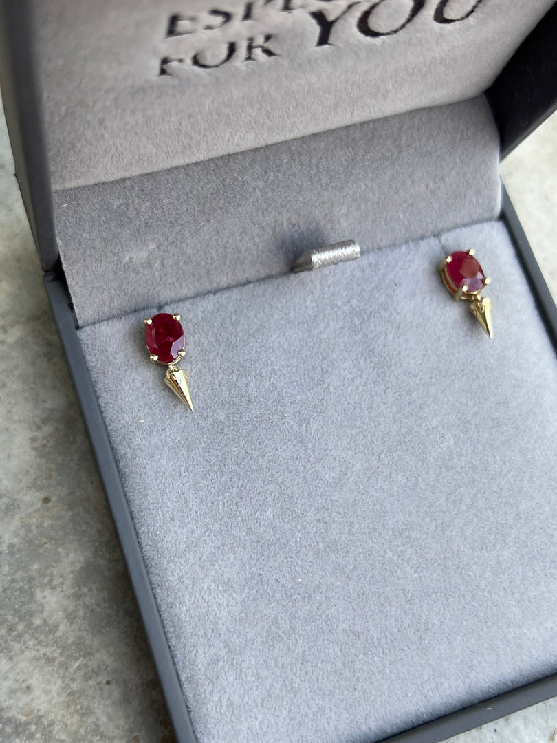 A pair of red gemstone earrings placed in a gray jewelry box with a black border.