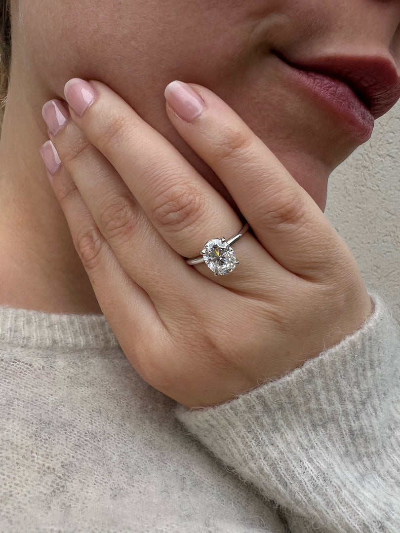 A close-up of a person's hand wearing a diamond engagement ring, with the ring's diamond visible.