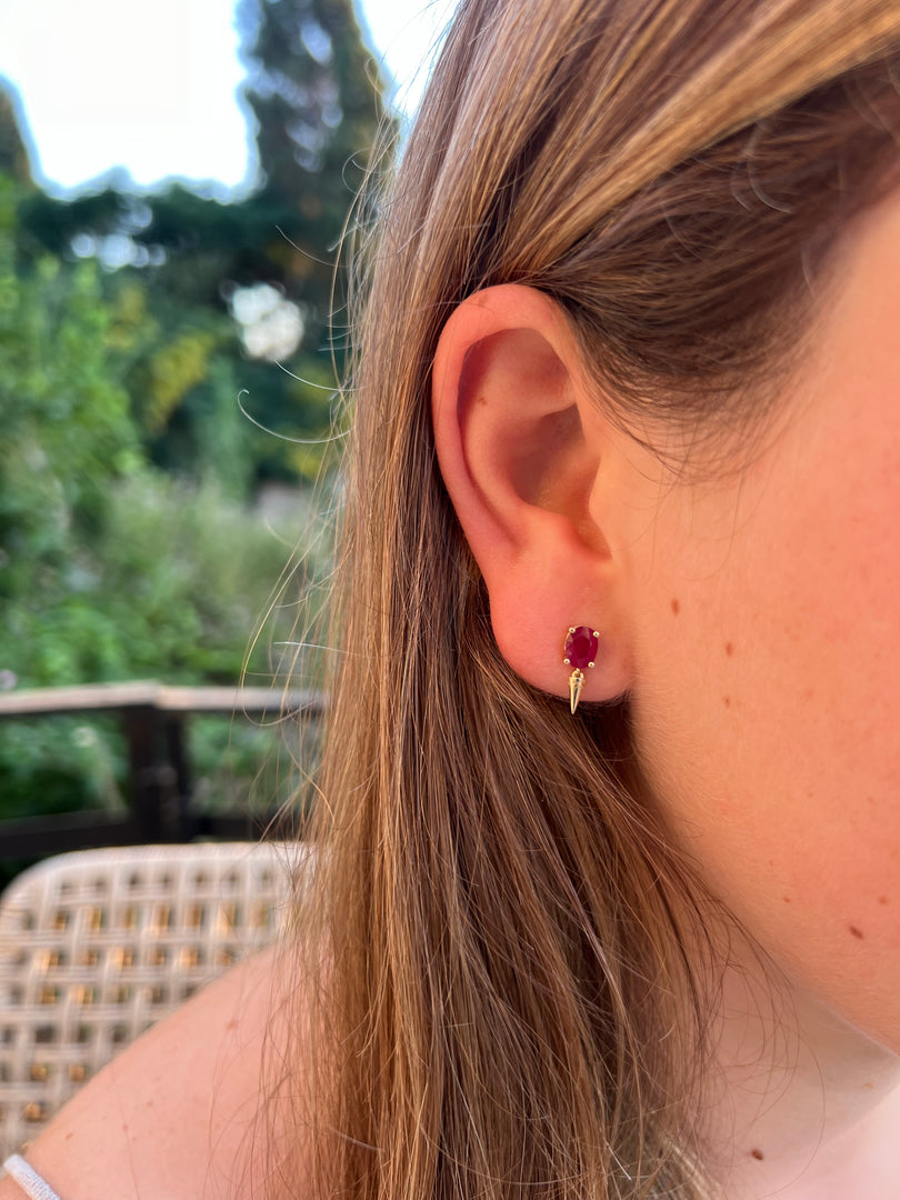 A close-up view of a person's ear with a small, red gemstone earring.