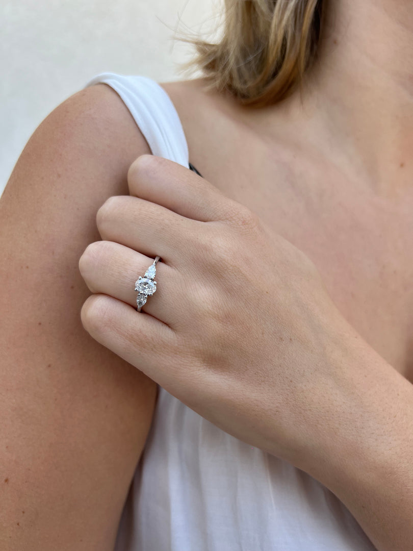 A close-up of a person's hand wearing a diamond engagement ring on the ring finger.
