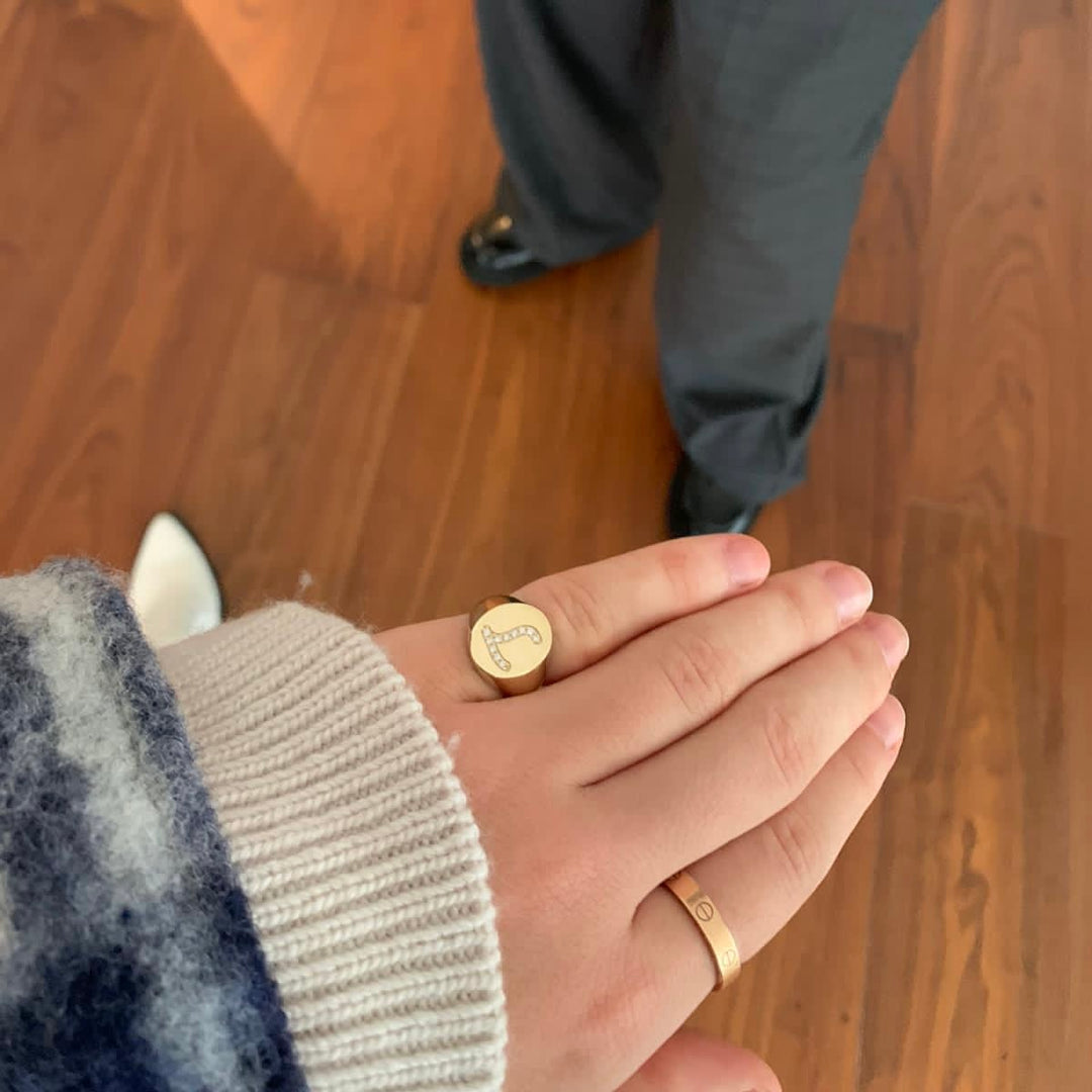 A close-up of a person's hand wearing two gold rings, one with a diamond design and the other with a simple band.
