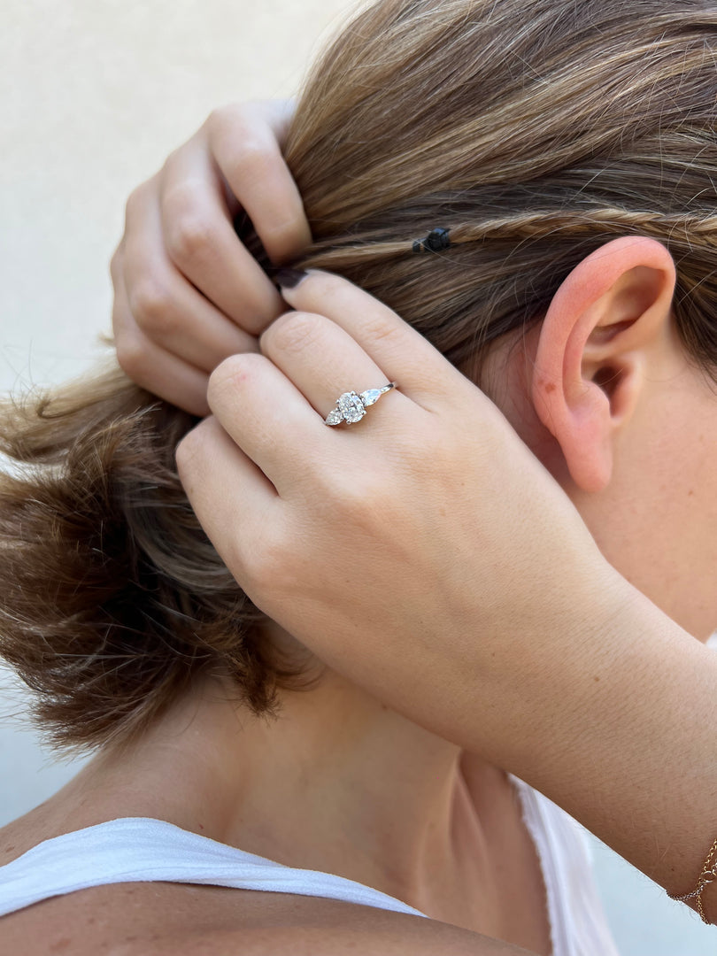 A close-up view of a person's hand adjusting their hair, with a diamond engagement ring visible on the finger.
