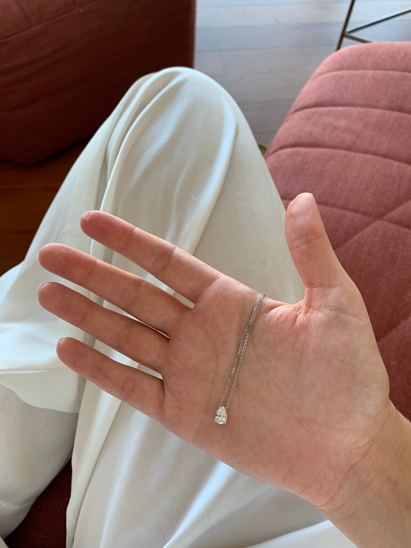 A hand holding a small piece of jewelry, possibly a necklace or bracelet, with a red cushion visible in the background.