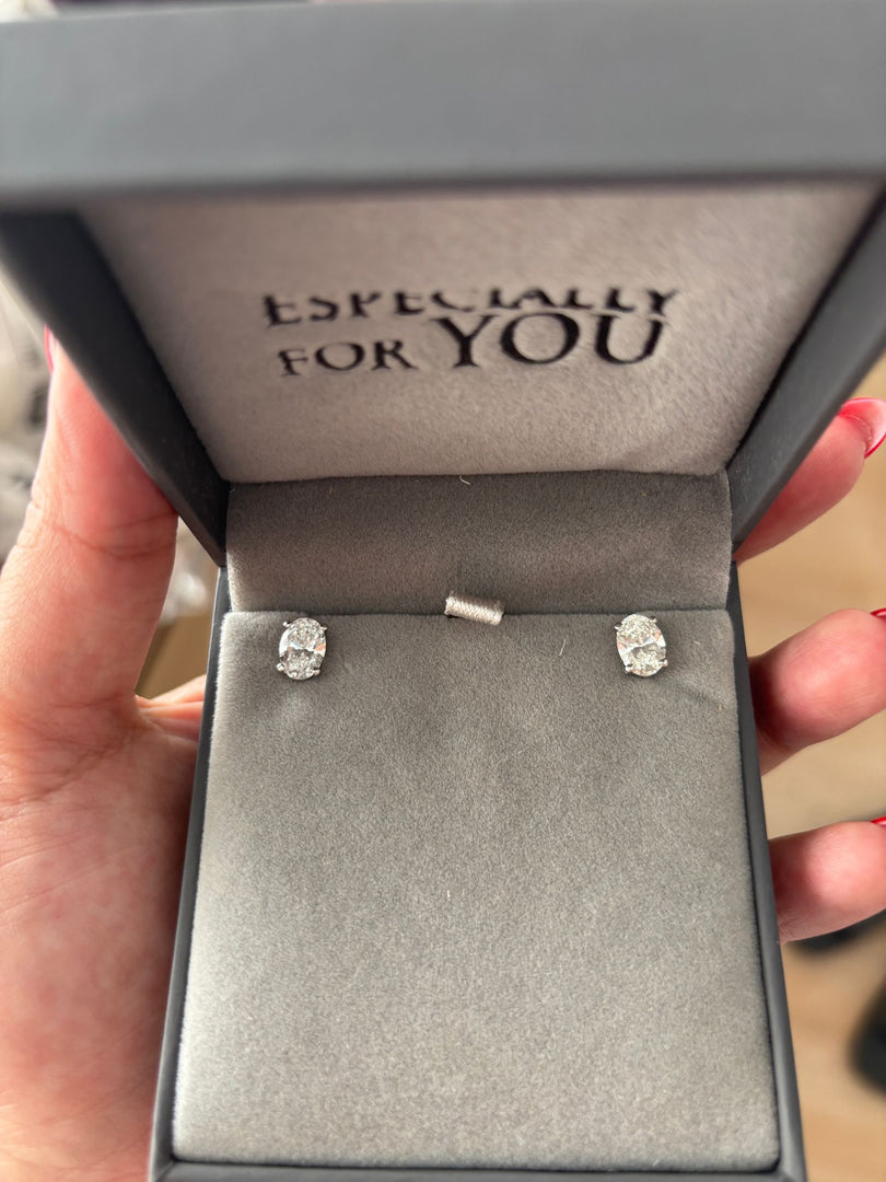 A hand holding a gray jewelry box with a pair of diamond earrings inside.