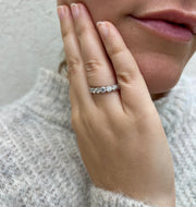 A close-up of a person's hand wearing a diamond ring, with a light gray sweater visible in the background.