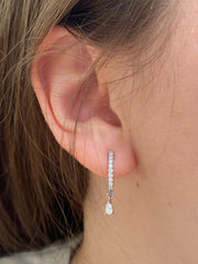 A close-up view of a person's ear adorned with a delicate earring featuring a dangling diamond.