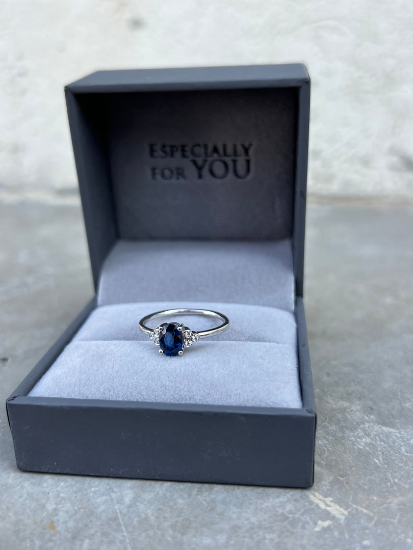 A silver ring with a blue gemstone is displayed in a black jewelry box with the text "ESPECIALLY FOR YOU" printed on it.