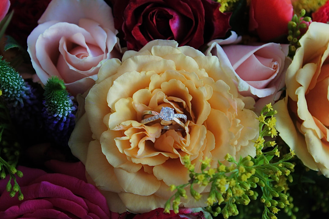 A close-up view of a bouquet of colorful flowers, including roses, carnations, and other blooms, with a ring visible in the center.