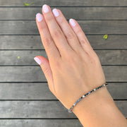 A hand with painted nails and a bracelet on a wooden surface.