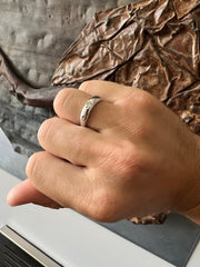 A close-up view of a person's hand wearing a ring, with a textured background that includes a brown fabric and a metal surface.