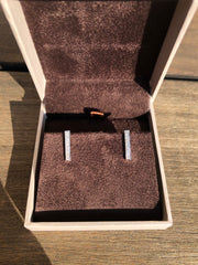a pair of diamond earrings placed inside a white jewelry box with a brown interior.