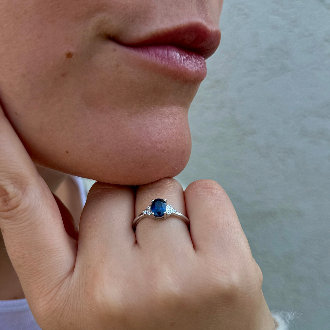 A close-up of a person's hand wearing a ring with a blue gemstone.