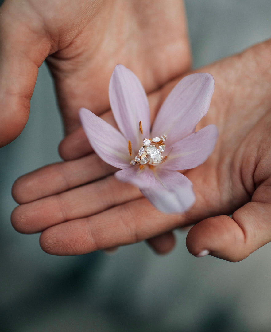 A close-up image of a person's hand gently holding a delicate pink flower with a diamond-encrusted center.