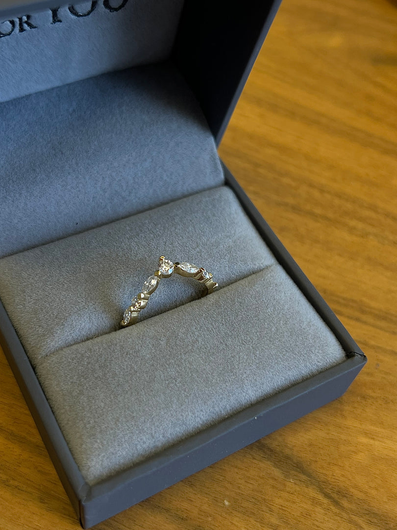 A gold ring with a diamond-encrusted band is displayed in a black jewelry box on a wooden surface.