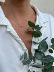 A close-up view of a person's neck and chest area, with a delicate necklace featuring a small diamond pendant and a branch of green leaves.