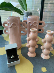 a table with three pink ceramic vases, a ring in a box, and a plant in the background.
