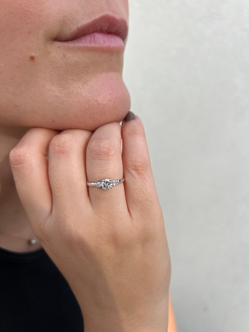 A close-up of a person's hand wearing a diamond ring, with a focus on the ring and the person's face.