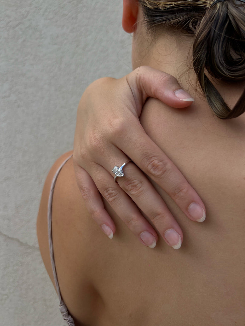 A close-up view of a person's hand wearing a diamond engagement ring, with the ring's diamond clearly visible.