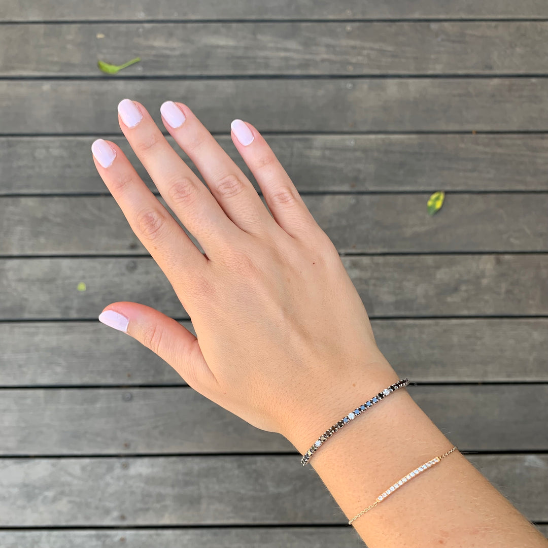 A hand with light pink nail polish and a bracelet on a wooden surface.