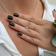 A close-up of a person's hand wearing a necklace with a diamond pendant and a ring on the ring finger.